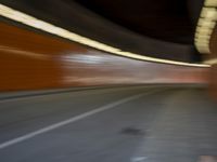 a man riding a skateboard down a city street next to a tall orange wall
