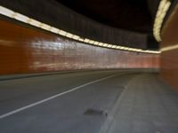 a man riding a skateboard down a city street next to a tall orange wall