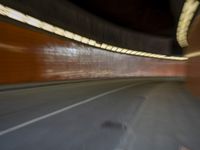 a man riding a skateboard down a city street next to a tall orange wall
