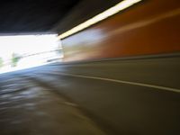 a man riding a skateboard down a city street next to a tall orange wall