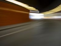 a man riding a skateboard down a city street next to a tall orange wall