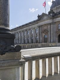 an old building with two flags in the background and steps leading up to it, and a statue on the ground below