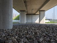 there is a pile of rocks underneath the bridge with a sky background the water near the structure has a long line of lines