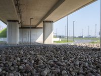 there is a pile of rocks underneath the bridge with a sky background the water near the structure has a long line of lines