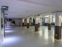 a long hall with wood pillars with white walls and windows on either side of the room