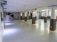 a long hall with wood pillars with white walls and windows on either side of the room