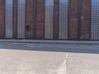 a man walking a white dog down the street by a large brick building with glass windows