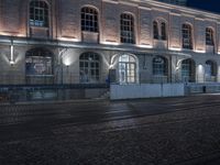 the entrance to a building that is lit up at night, with cars parked in front