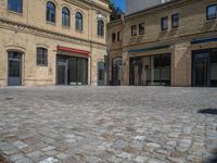 the sidewalk is paved with stones and has a bench in front of it, with no people inside