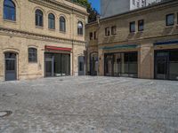 the sidewalk is paved with stones and has a bench in front of it, with no people inside