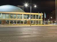 a large building on a street in an empty parking lot at night time with cars passing by