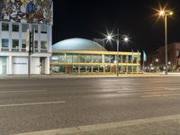 a large building on a street in an empty parking lot at night time with cars passing by