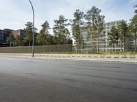 two buildings along the street beside a long fence and the road next to them is empty with trees