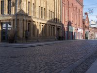 the street is empty and has bricks on it as well as a brick building with windows