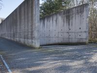 a long concrete wall on the side of the road near some trees and a gravel road