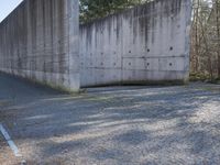 a long concrete wall on the side of the road near some trees and a gravel road