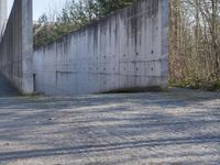 a long concrete wall on the side of the road near some trees and a gravel road