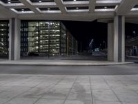 a very large modern office building lit up at night by the sidewalk area outside of the building