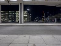 a very large modern office building lit up at night by the sidewalk area outside of the building