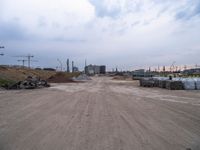 a dirt road going to construction next to some buildings on a hill under a cloudy sky