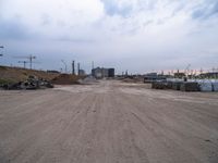 a dirt road going to construction next to some buildings on a hill under a cloudy sky