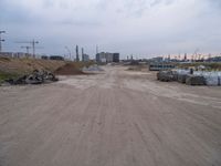 a dirt road going to construction next to some buildings on a hill under a cloudy sky