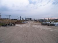 a dirt road going to construction next to some buildings on a hill under a cloudy sky