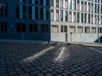 an empty cobblestone street with a blue building in the background and a light shine on the sidewalk