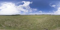 a panoramic view of a grassy field with clouds in the sky above it