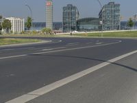 the street with two cars is empty in front of some city buildings by water in a sunny day