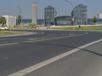 the street with two cars is empty in front of some city buildings by water in a sunny day