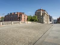 people walking across a bridge in front of buildings in a city setting with cobblestones