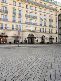 people walking on sidewalk in front of an old hotel building with large windows and doors