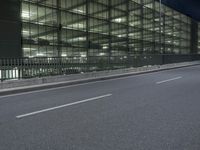 a paved road with a parking garage next to it at night - night - time