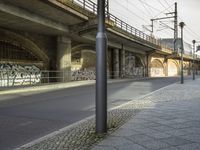 an overpass above a street with several graffiti on it's wall and a sidewalk with cobblestones