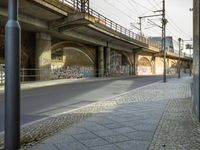 an overpass above a street with several graffiti on it's wall and a sidewalk with cobblestones