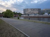 people sit on the shore next to the water in a city park next to the river and buildings