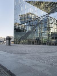 a large modern building is reflecting the modern architecture behind it, there is a concrete sidewalk