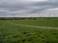 a green field with two small roads running across it and wind turbines behind the grass