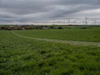 a green field with two small roads running across it and wind turbines behind the grass