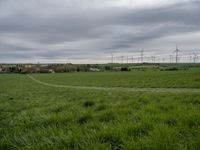 a green field with two small roads running across it and wind turbines behind the grass