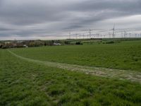 a green field with two small roads running across it and wind turbines behind the grass