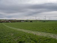 a green field with two small roads running across it and wind turbines behind the grass