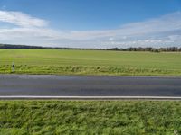 the landscape of an open highway with a lone person walking on the road next to the large field