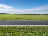 the landscape of an open highway with a lone person walking on the road next to the large field