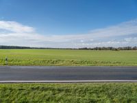 the landscape of an open highway with a lone person walking on the road next to the large field