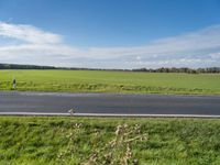 the landscape of an open highway with a lone person walking on the road next to the large field