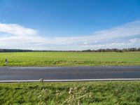 the landscape of an open highway with a lone person walking on the road next to the large field