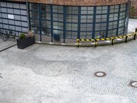 a yellow sign and people walk past the building in a circle that has windows and a bench