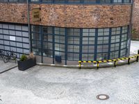 a yellow sign and people walk past the building in a circle that has windows and a bench